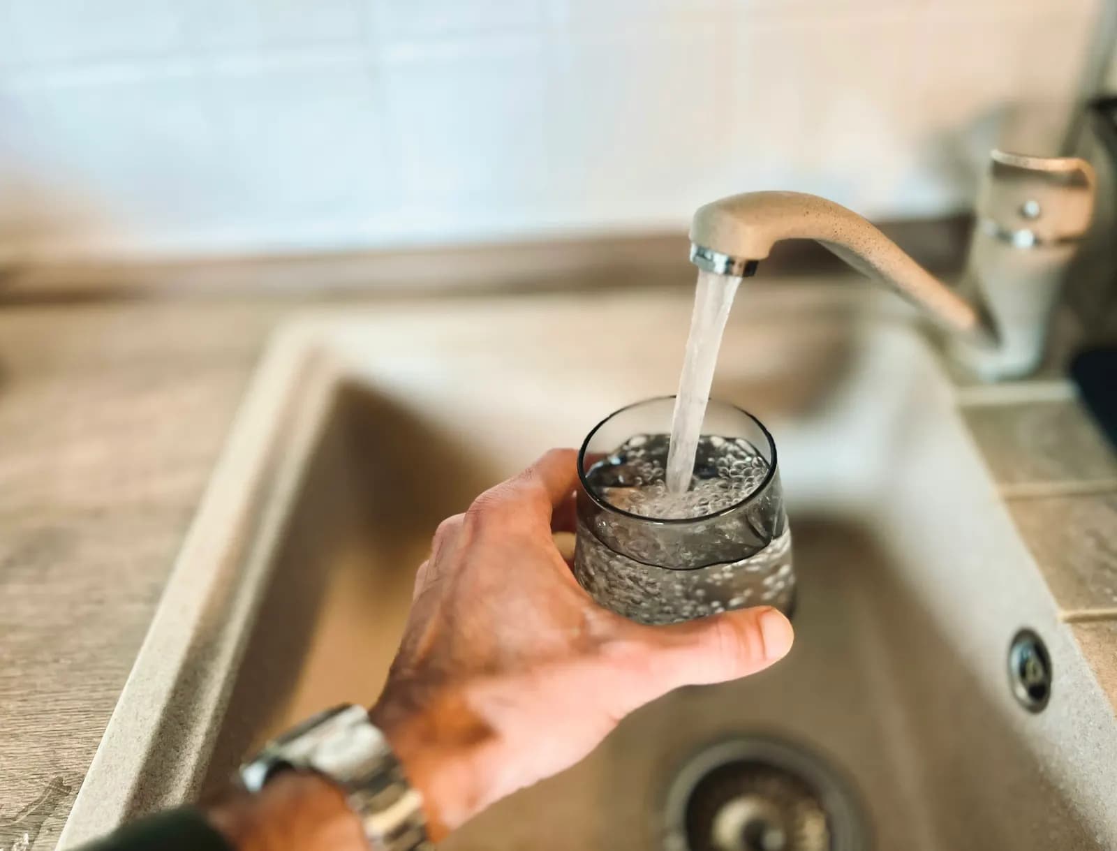 Vaso llenándose de agua bajo el grifo de un fregadero