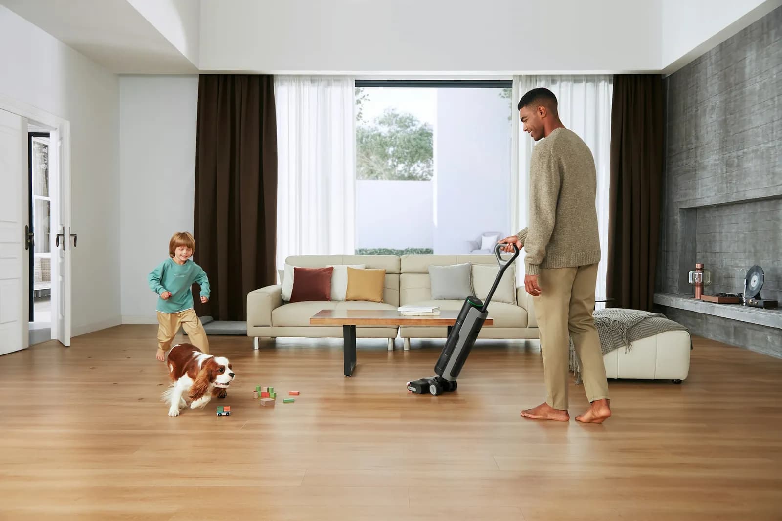 Hombre pasando la aspiradora en un salón luminoso mientras los niños y los perros juegan